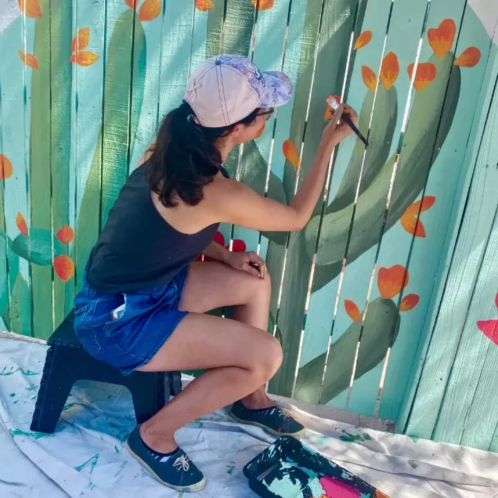 Brigitte De Marco painting flowering prickly pear on the Garfield fence mural