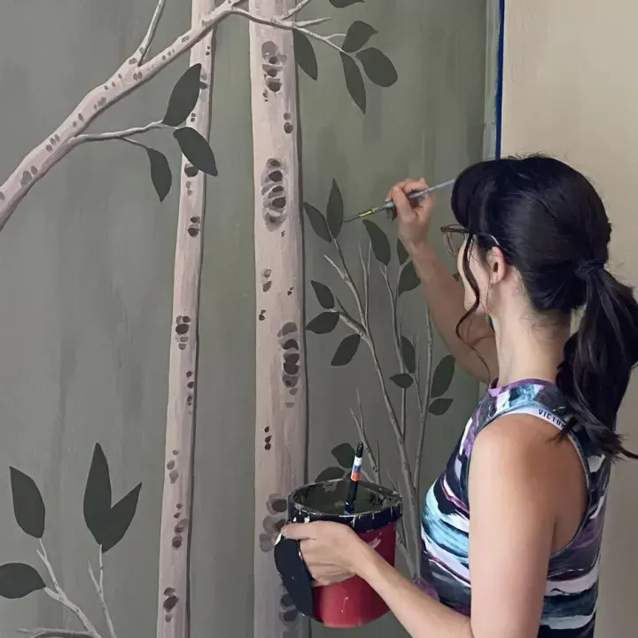 Brigitte De Marco painting an interior aspen forest mural