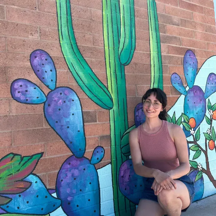 Brigitte De Marco seated in front of her saguaro and prickly pear brick wall mural