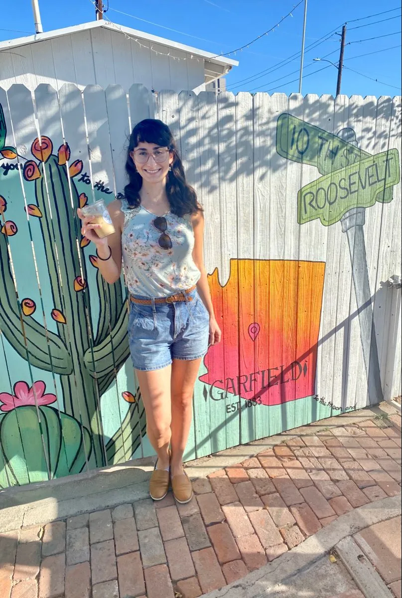 Brigitte with an iced coffee in front of the fence